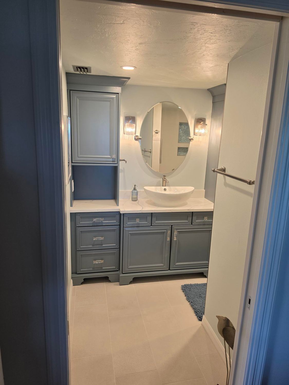 Blue bathroom with vanity, oval mirror, and white sink viewed from the doorway.