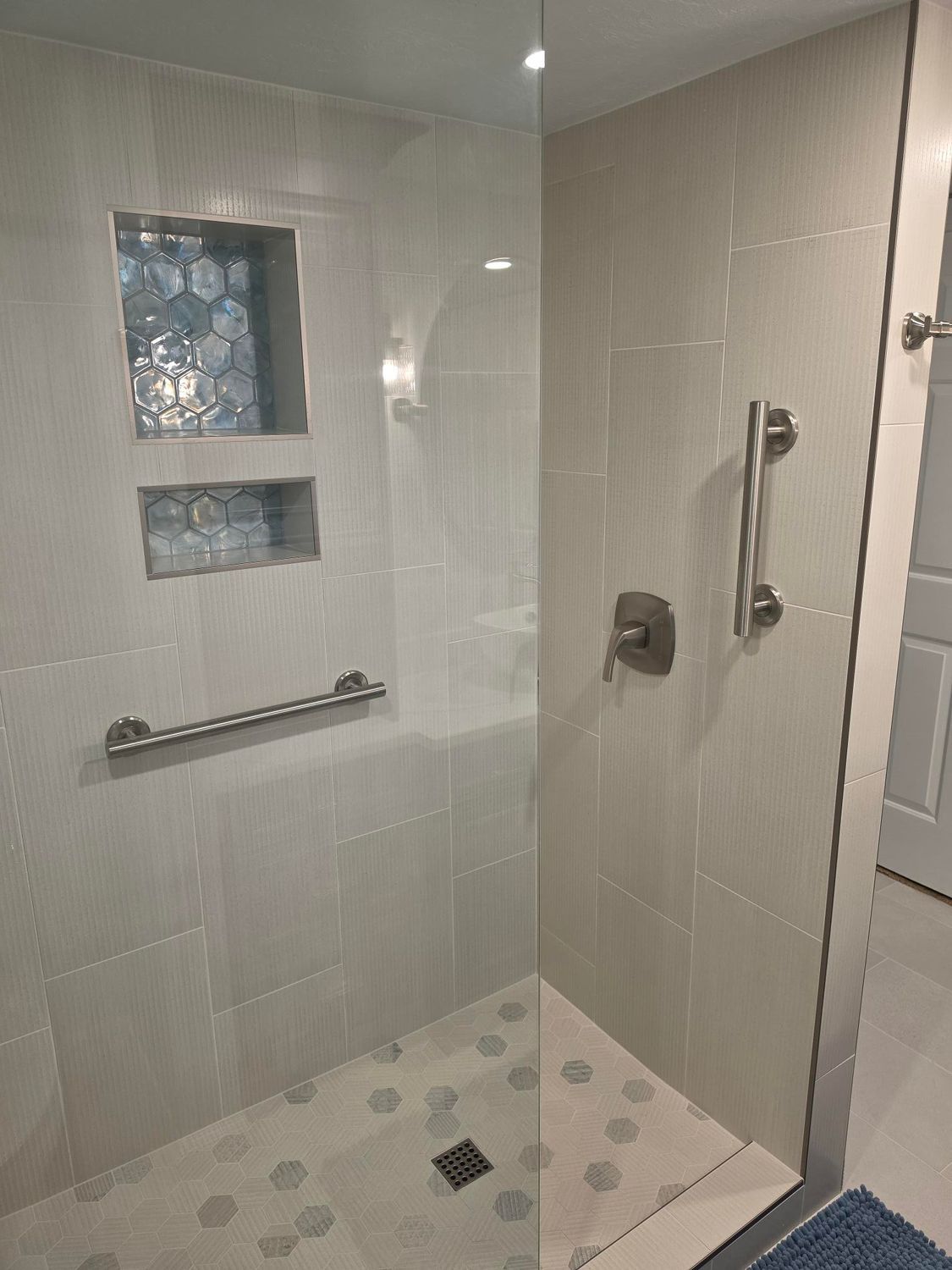 Modern walk-in shower with white tile, pebble floor, glass partition, and built-in wall niches