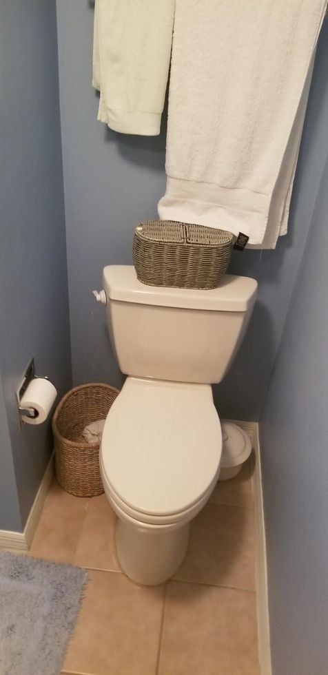 Small bathroom with toilet, woven baskets, and white towels hanging above the tank.