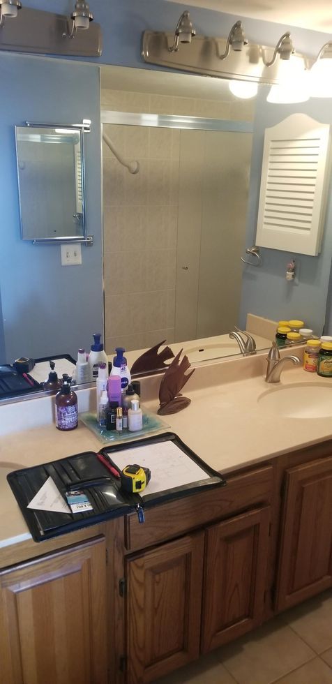 Bathroom vanity with mirror, sink, toiletries, and wooden cabinets under wall lights.