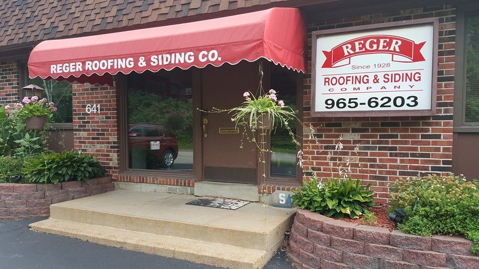 Brick storefront of Reger Roofing & Siding Co. with a red awning and hanging flower baskets near the entrance.