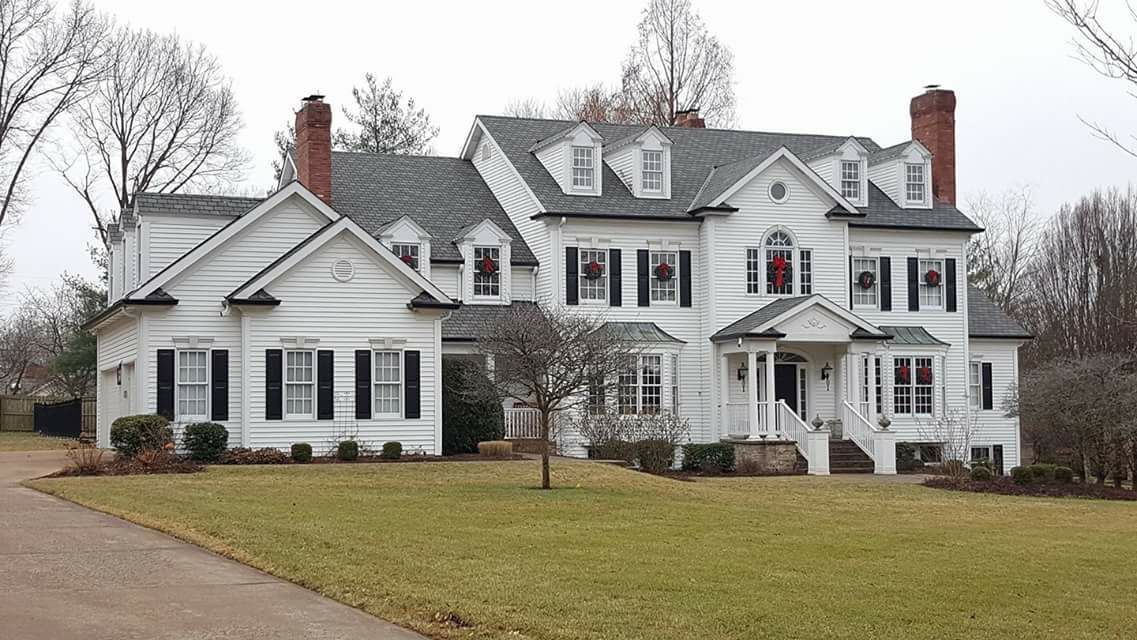 A large, two-story white house with black shutters, multiple gables, and chimneys, set on a grassy lawn.