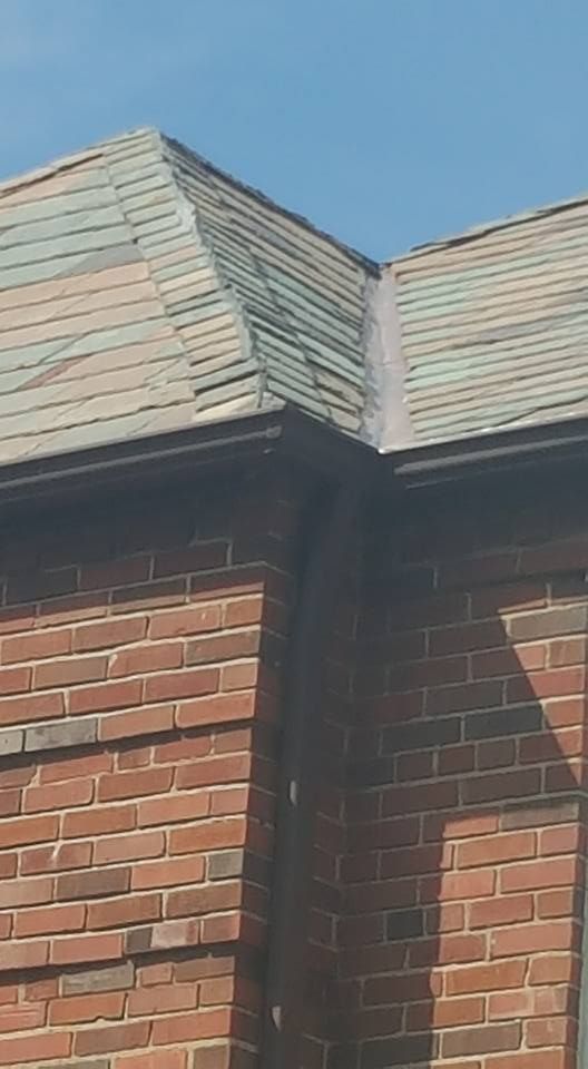 The corner of a brick building with a gray slate roof and dark metal gutters.
