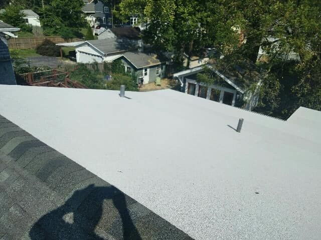 A white, flat roof surface with two small pipes, viewed from above, with dark shingles in the foreground.