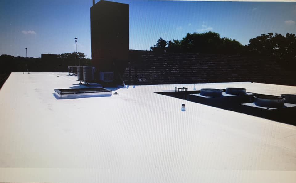 A flat roof with a white membrane surface, featuring several HVAC units, a large vent, and a brown brick structure.