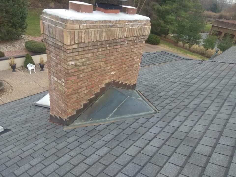 A brick chimney rising through a dark gray shingled roof, featuring a triangular glass skylight built into its side.