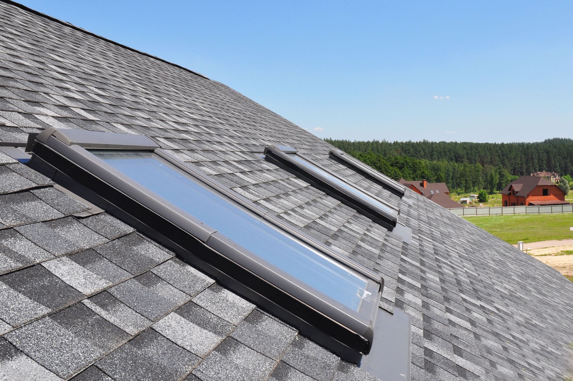 Two roof windows with dark frames installed on a sloped roof with gray shingles against a clear blue sky.