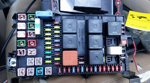 Fuse box with various colored fuses and black relays, a yellow manual, and exposed wires.