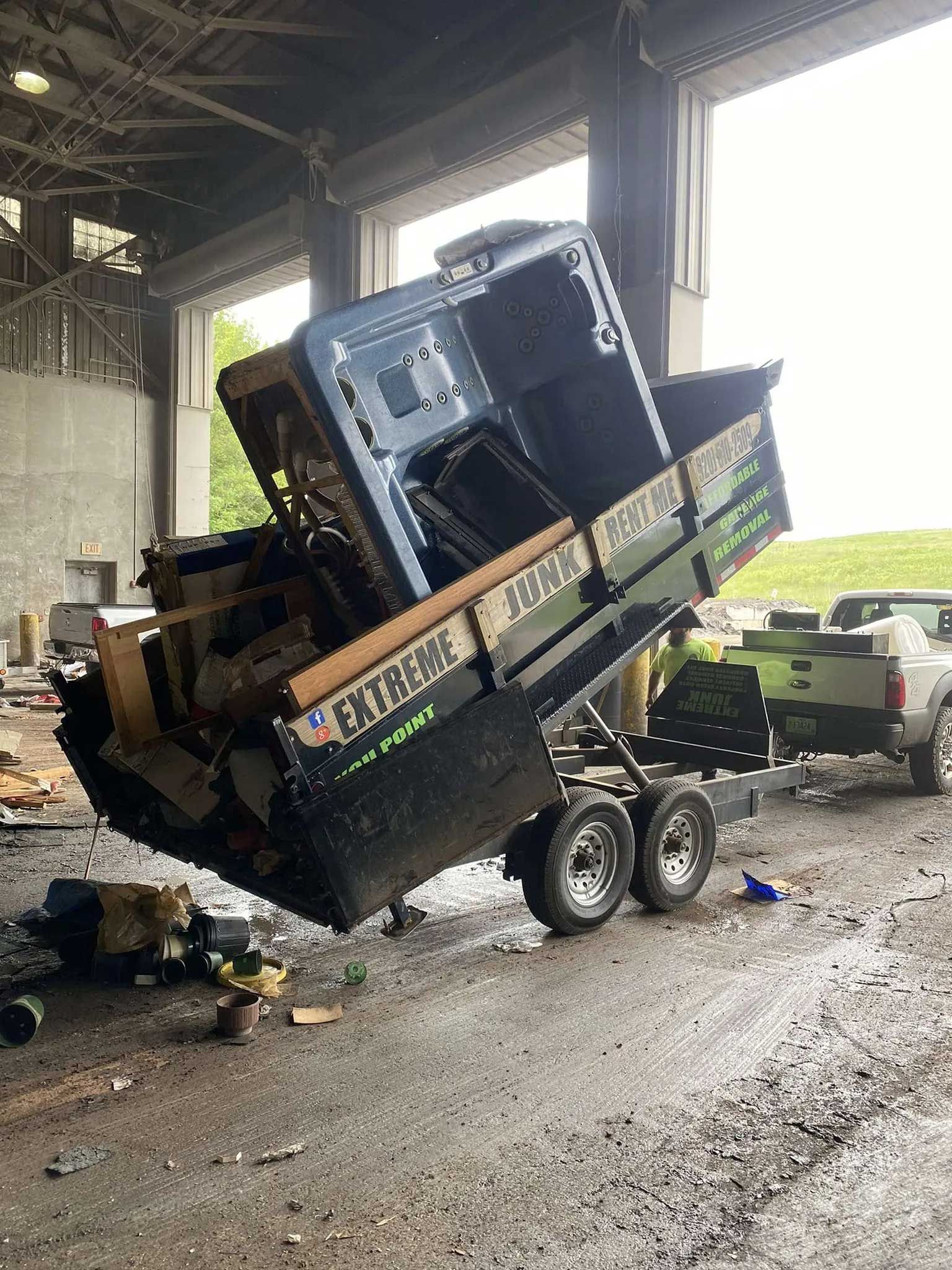 A black dump trailer tipped upright in a shed, carrying a large blue metal cabinet, hitched to a white pickup truck.