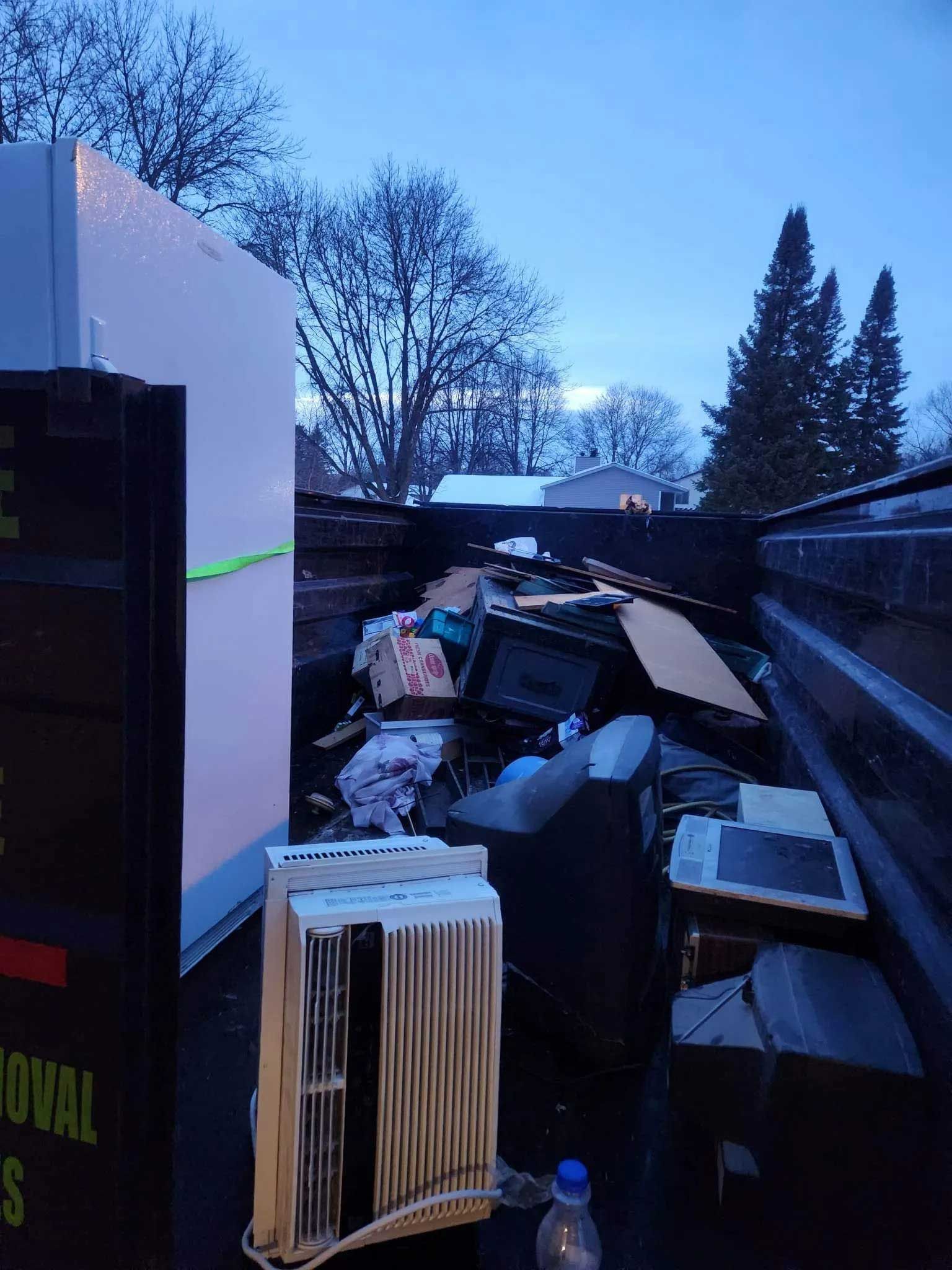 The bed of a truck filled with discarded items, including a white refrigerator and a window air conditioning unit.