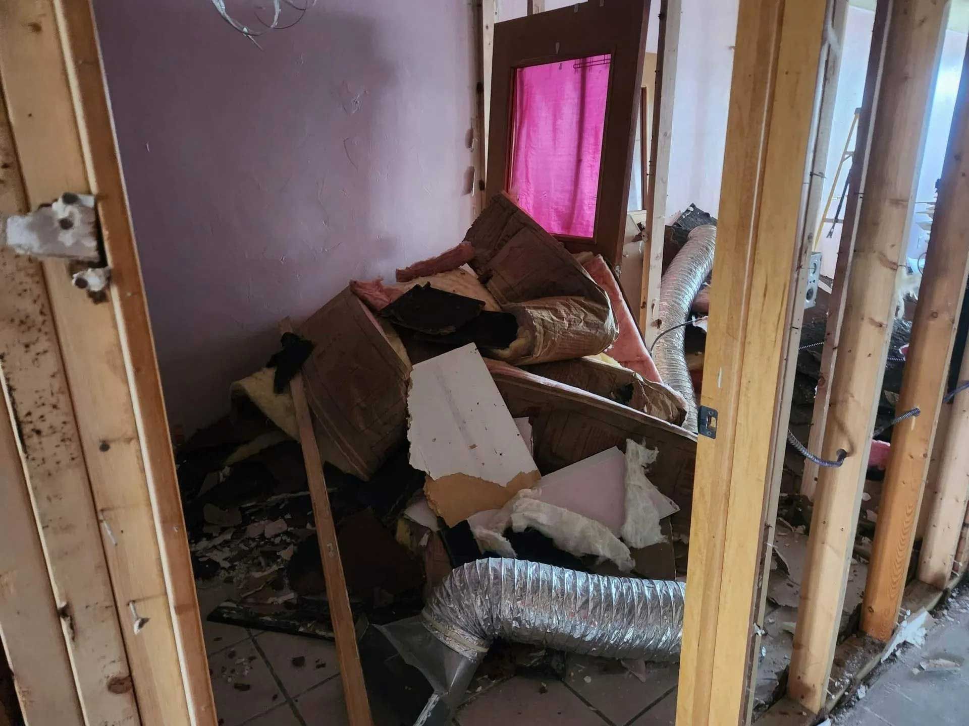 Interior view of a room under renovation with bare wood wall studs, debris, and silver flexible ventilation ducting.