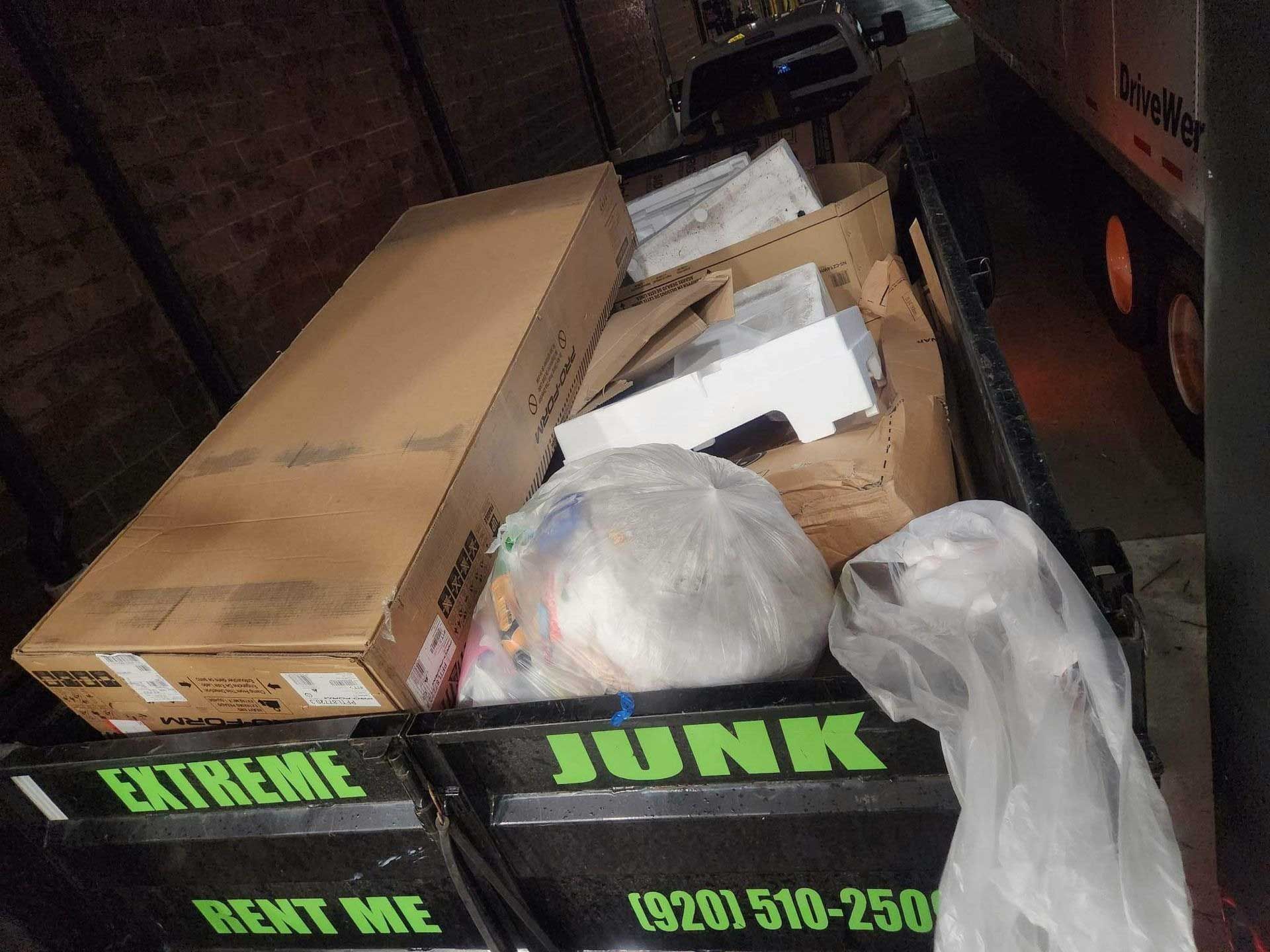 A black rental dumpster filled with cardboard boxes and trash bags, with 