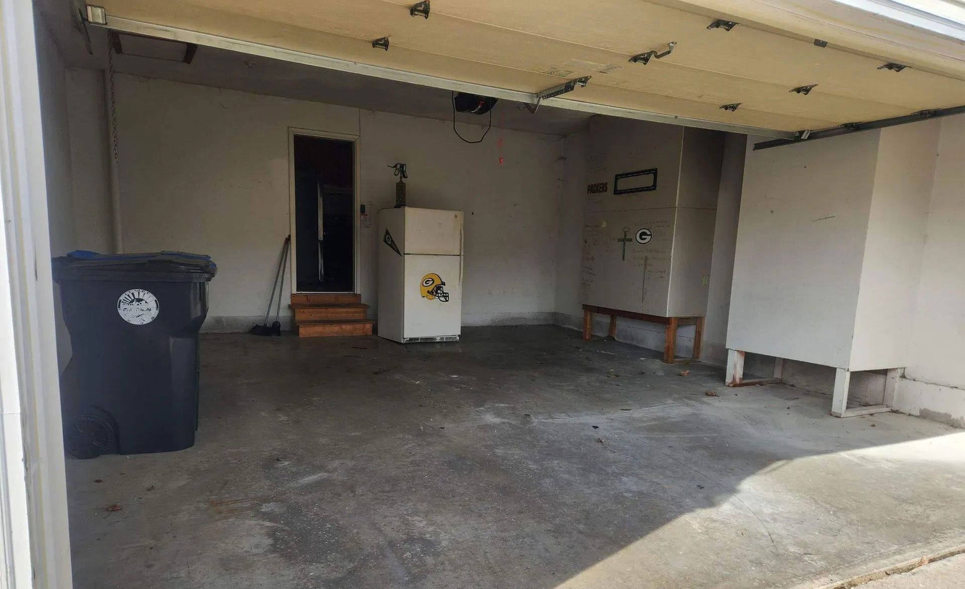 A view into a sparse, open garage featuring a black trash bin, a white upright freezer, and a metal storage cabinet.