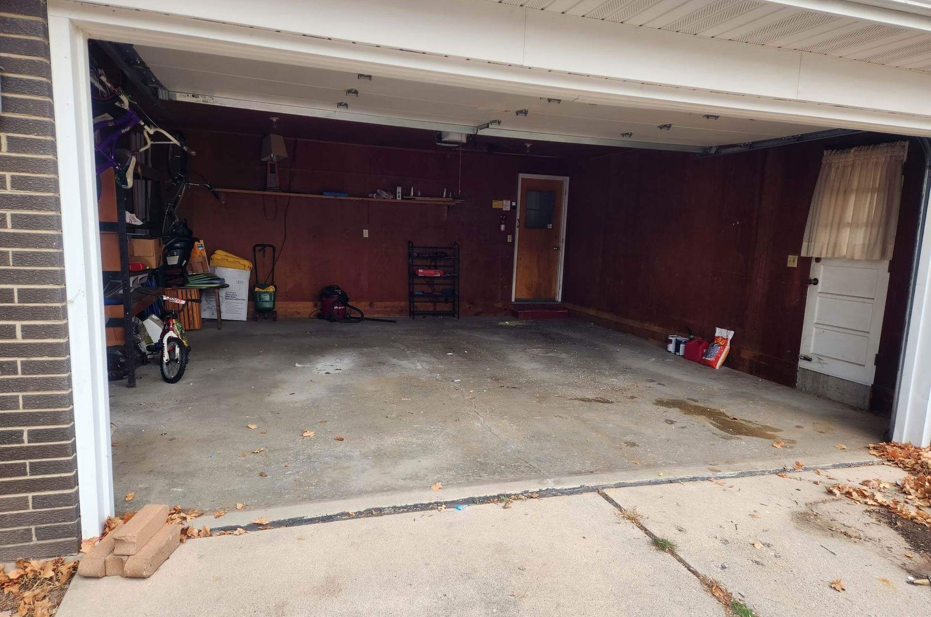 An open residential garage with dark walls, a concrete floor, a bicycle on the left, and a white door on the right.