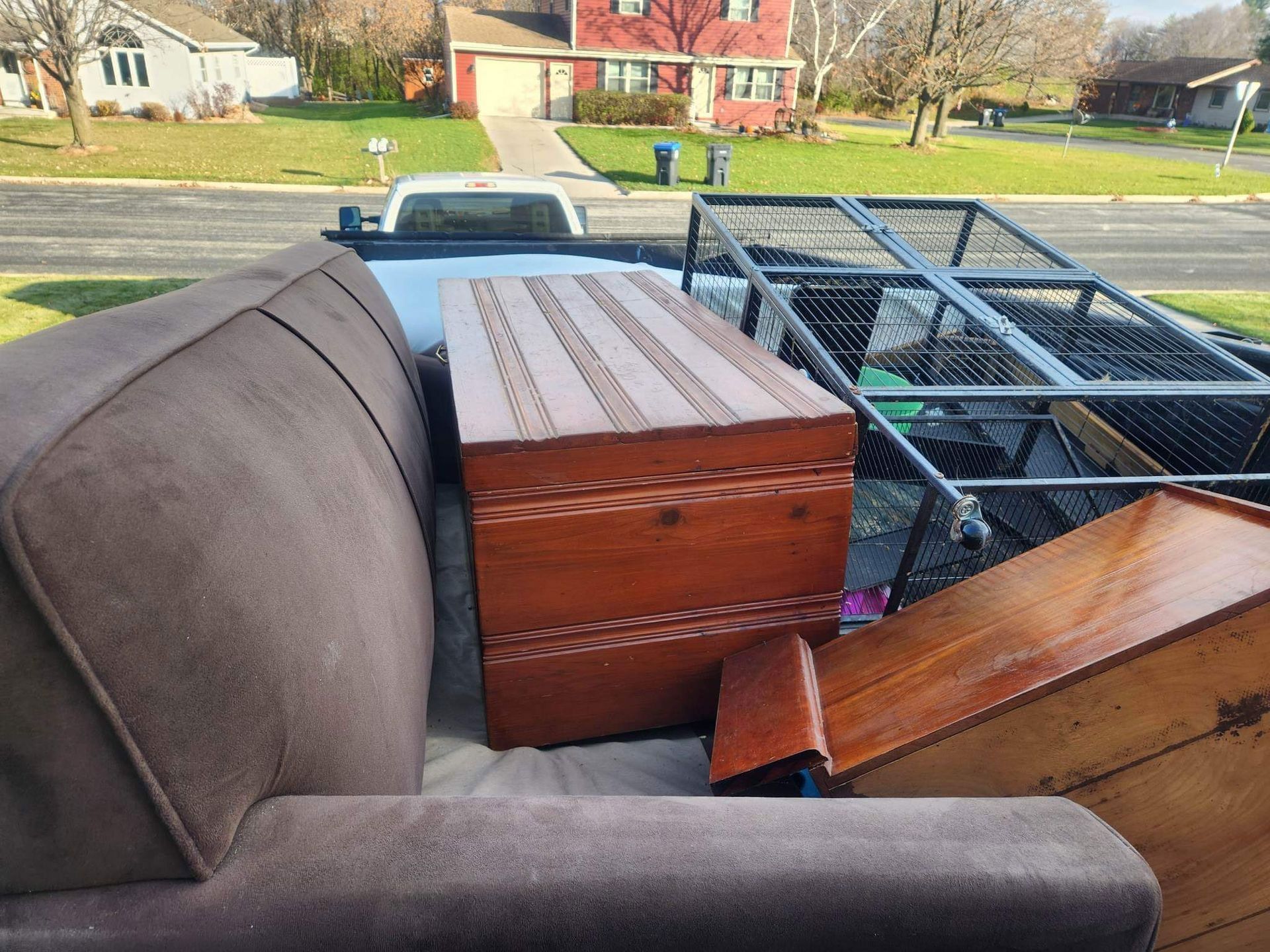 A brown sofa, a wooden chest, and a metal trailer frame are packed into the back of a pickup truck on a sunny day.