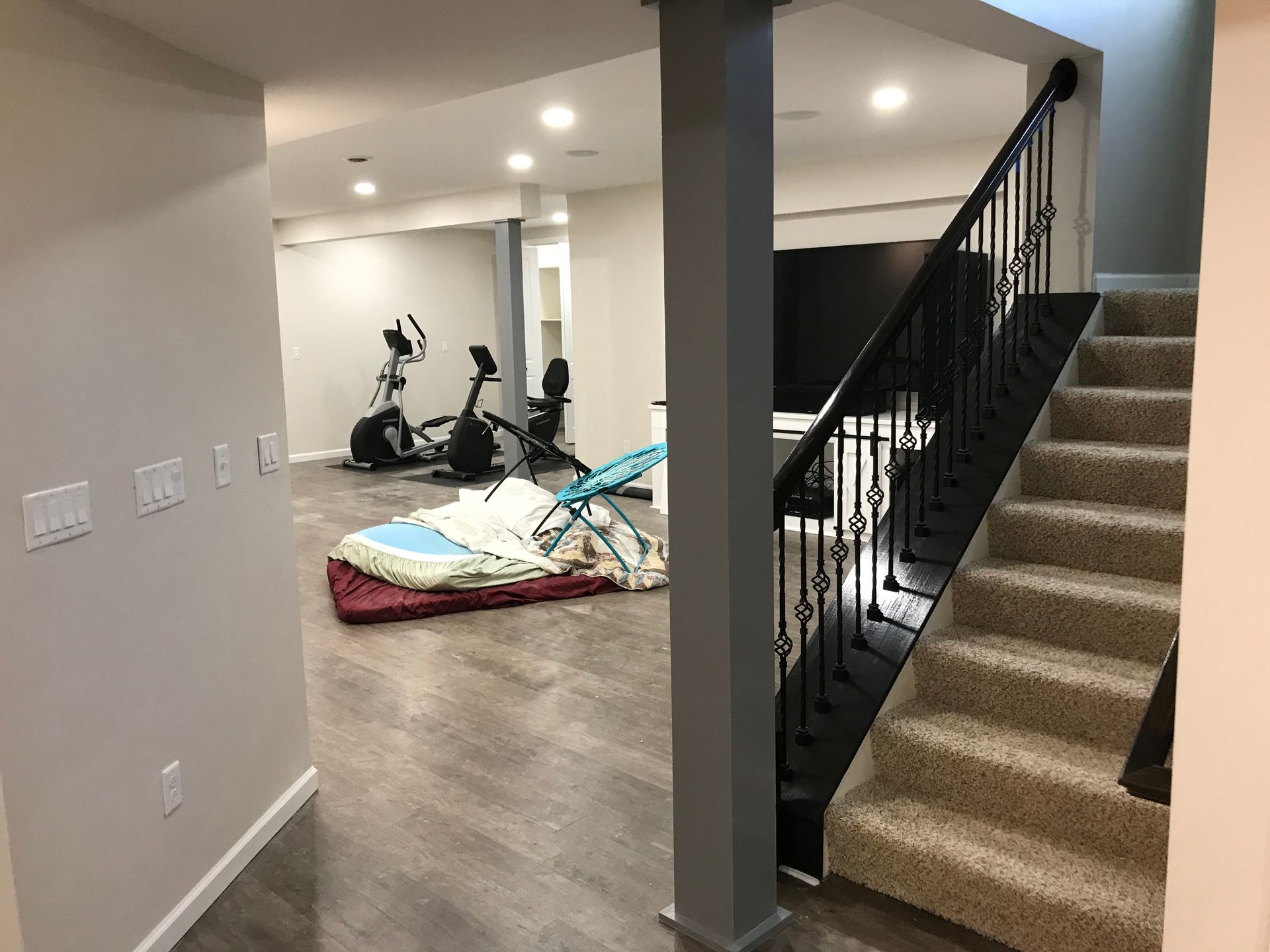 Basement interior: stairs, exercise equipment, and a support beam.