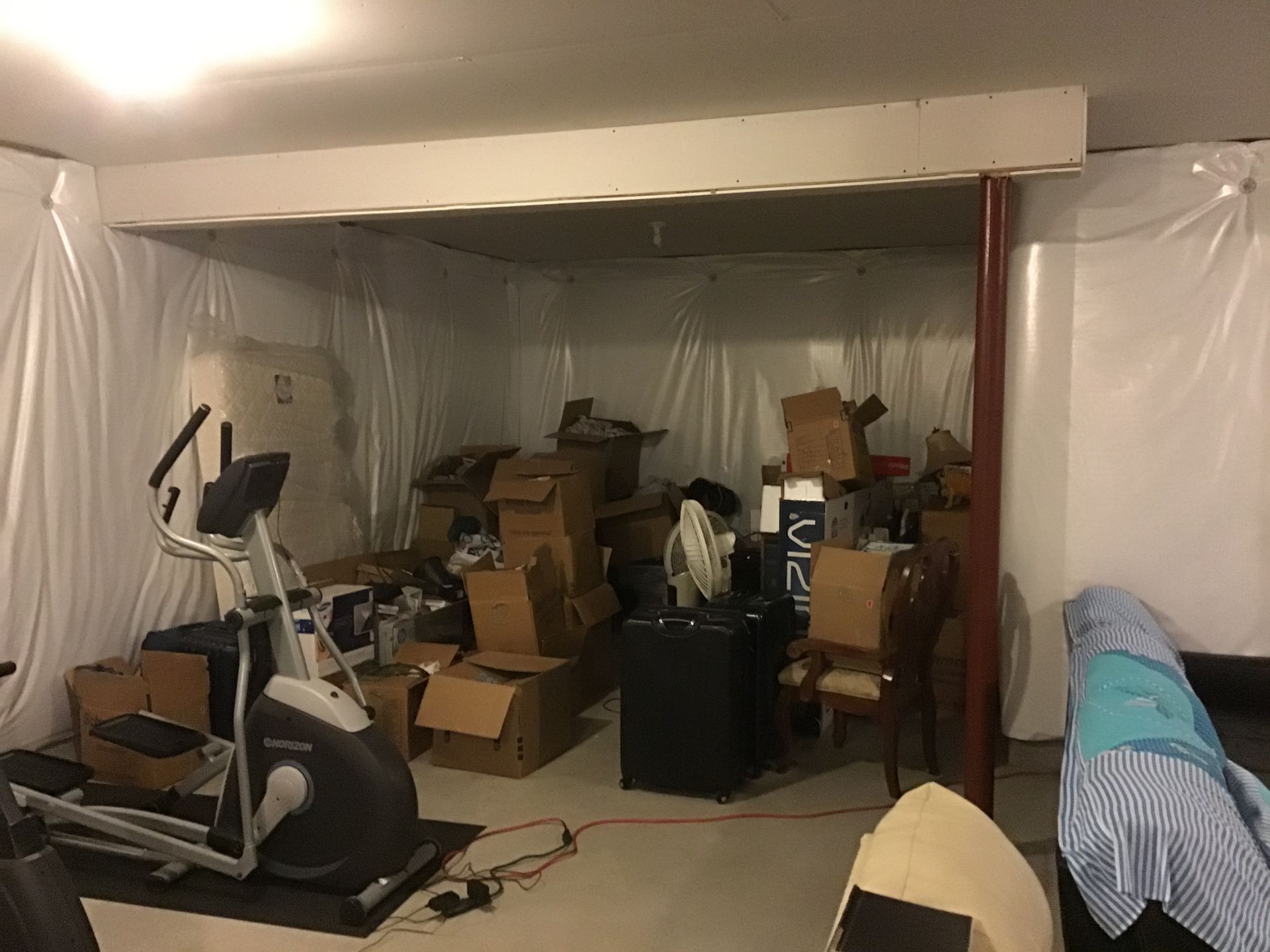 Basement storage area with an exercise machine, boxes, and a beam.