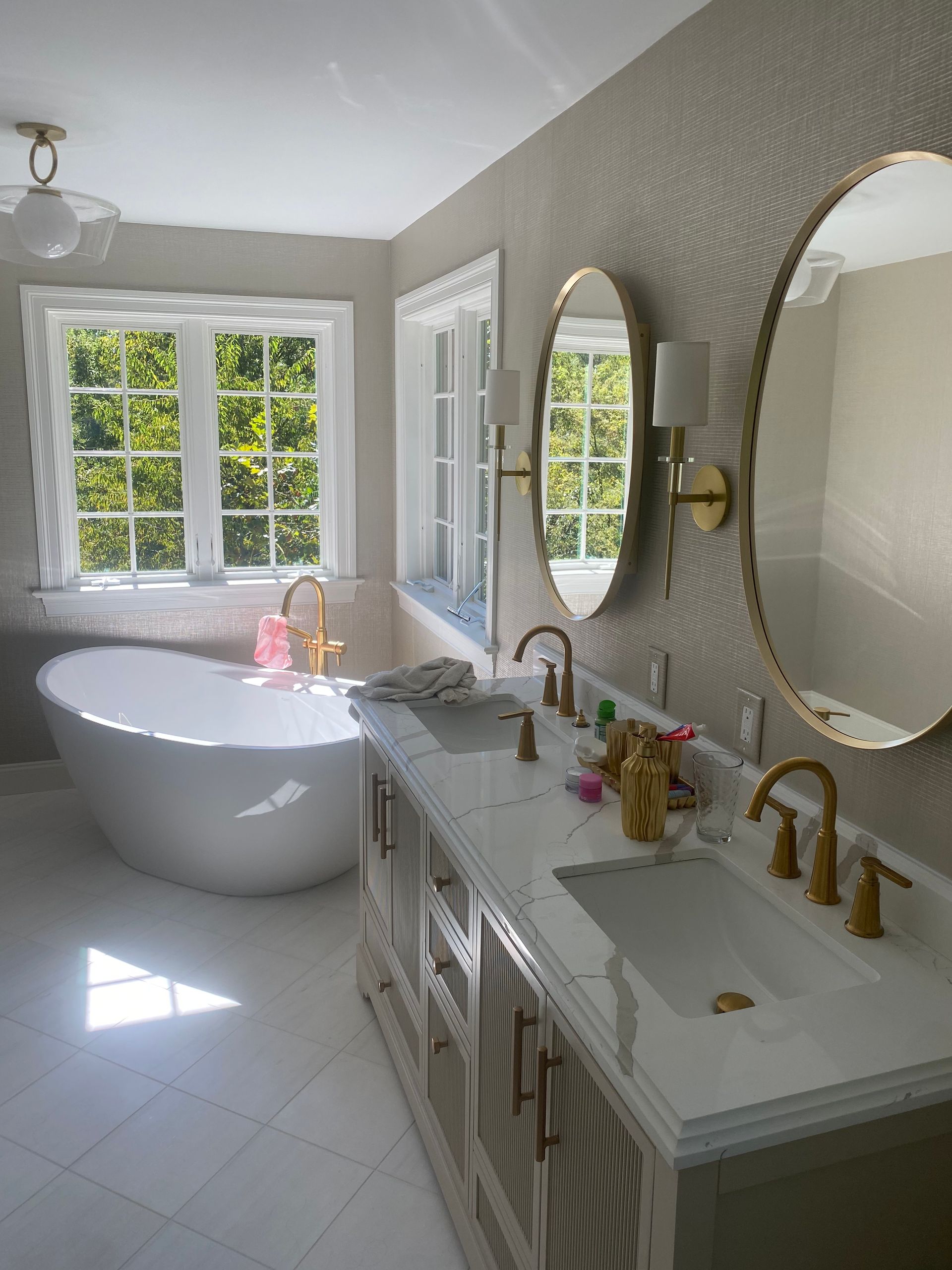 Luxurious bathroom with soaking tub, double vanity, oval mirrors, and gold fixtures.