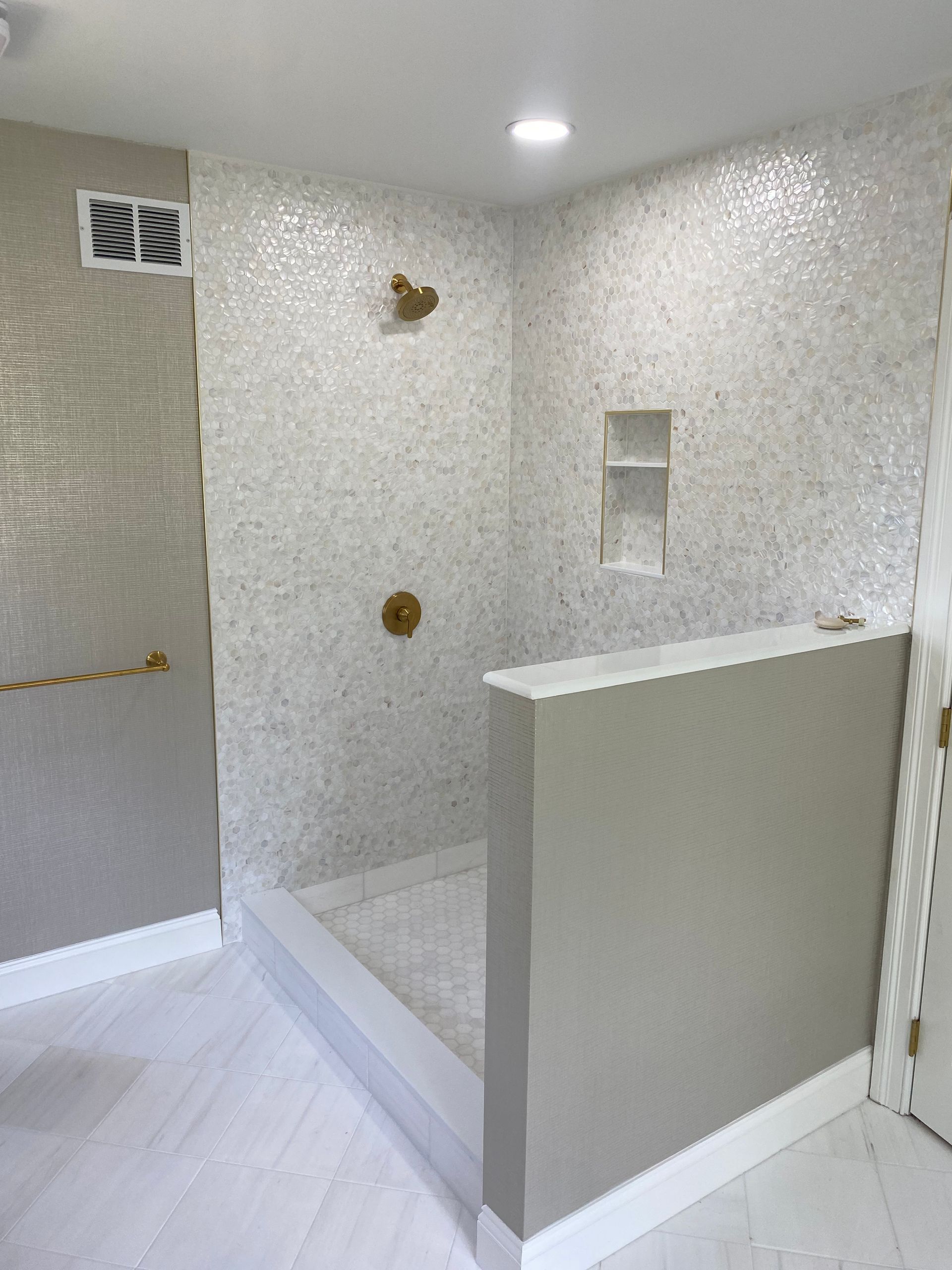 Modern shower with white mosaic tile walls, gold fixtures, and a gray half-wall.