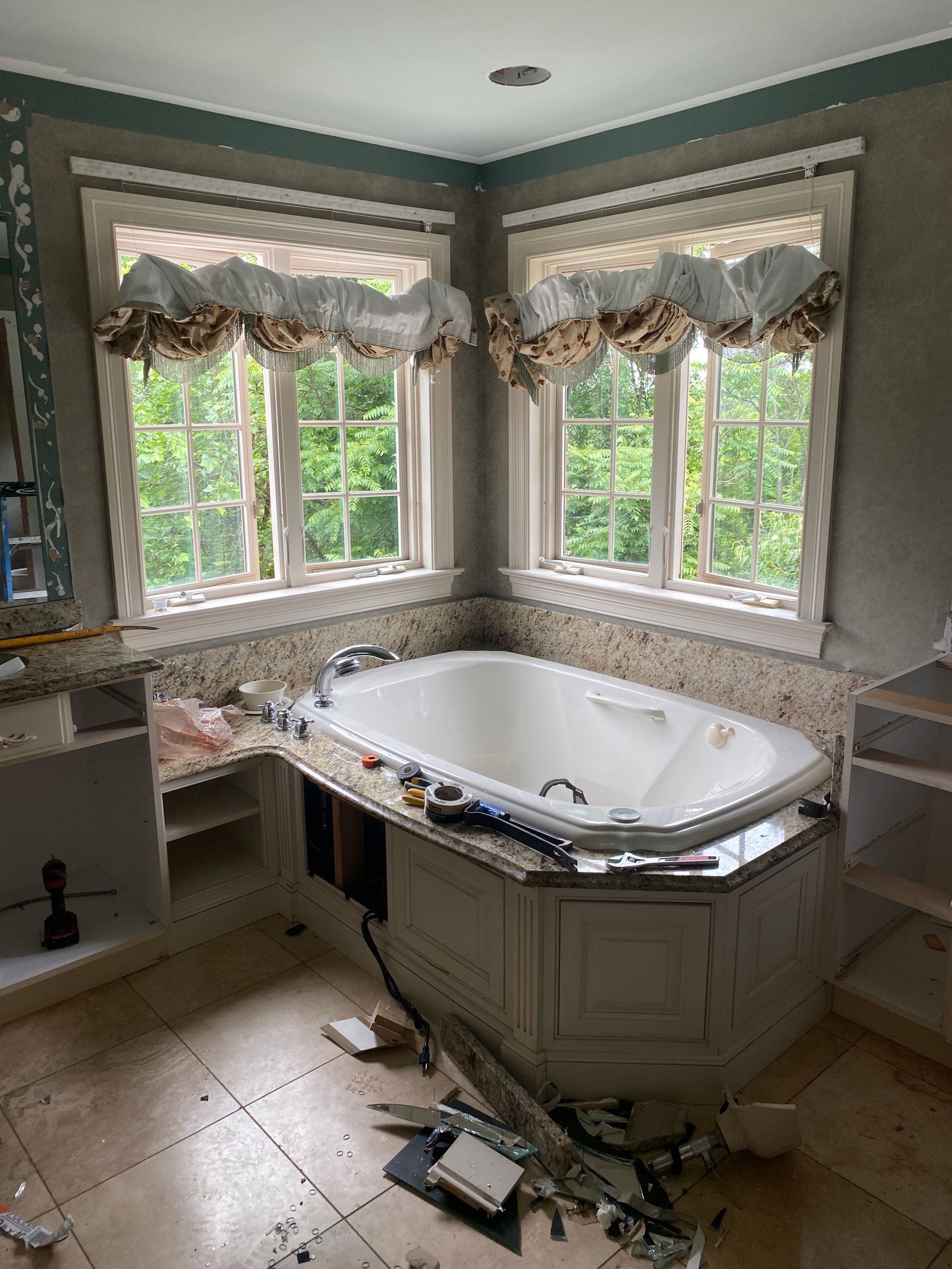 Bathroom with corner tub under windows, undergoing renovation. Debris on floor.