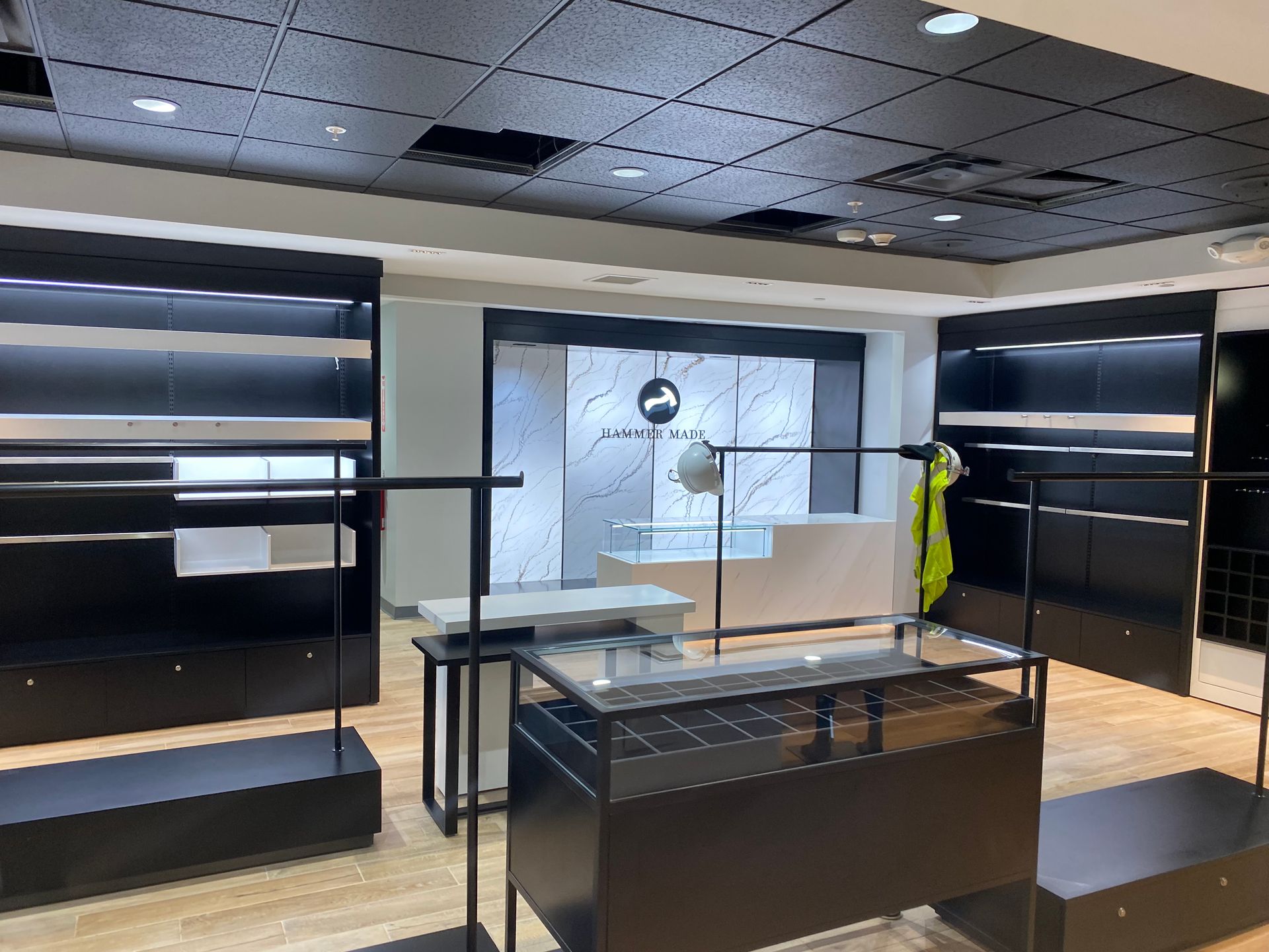 Inside a clothing store, black shelves and displays with merchandise are set against a white wall.