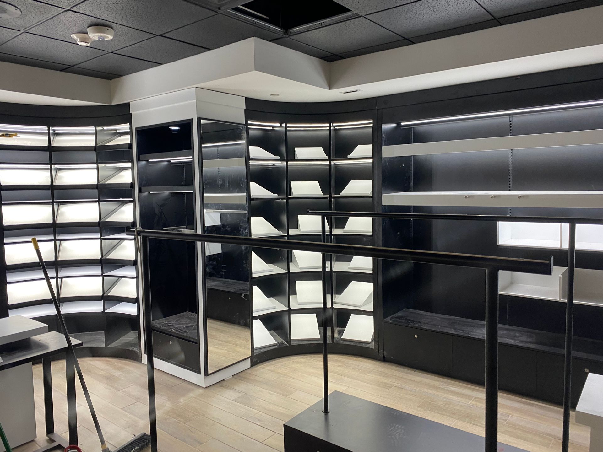 Empty retail space with black shelving and display racks; light-colored wooden floor.