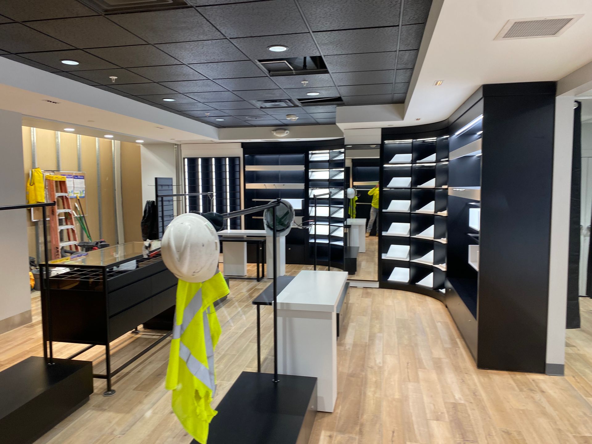 Interior view of a store under construction; a white hard hat and yellow vest hang from a display.