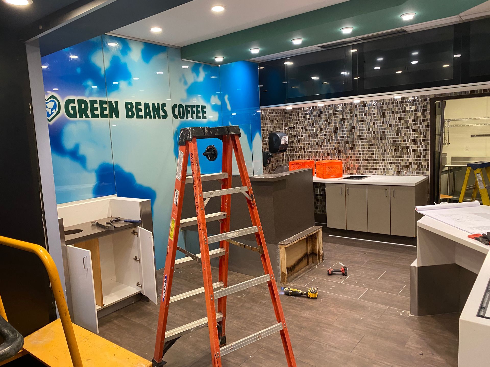 Interior of a Green Beans Coffee store under construction. Ladder, cabinets, and branding are visible.