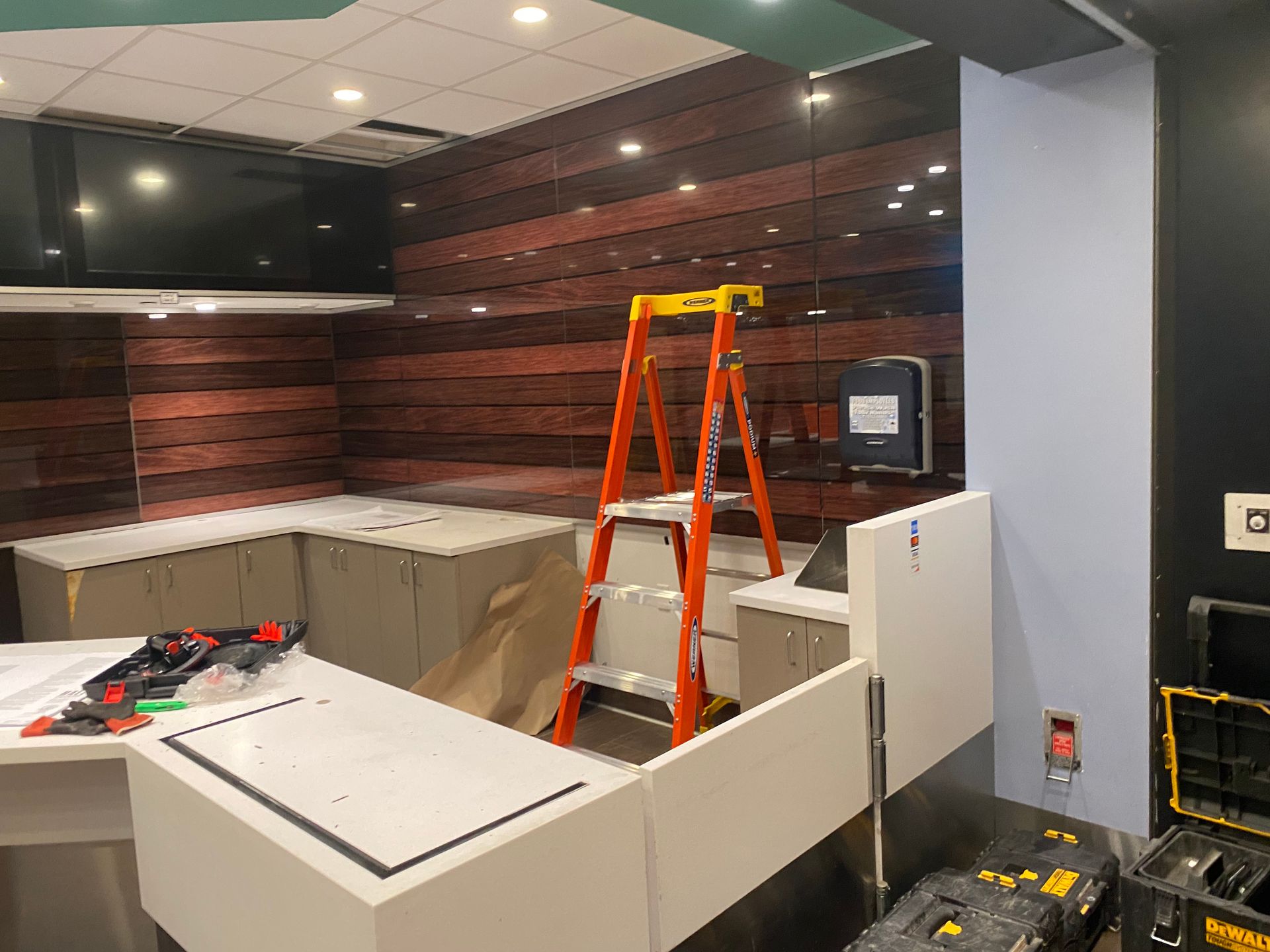 Construction site interior: a ladder stands near a partially built white countertop. Wooden paneling on the wall.