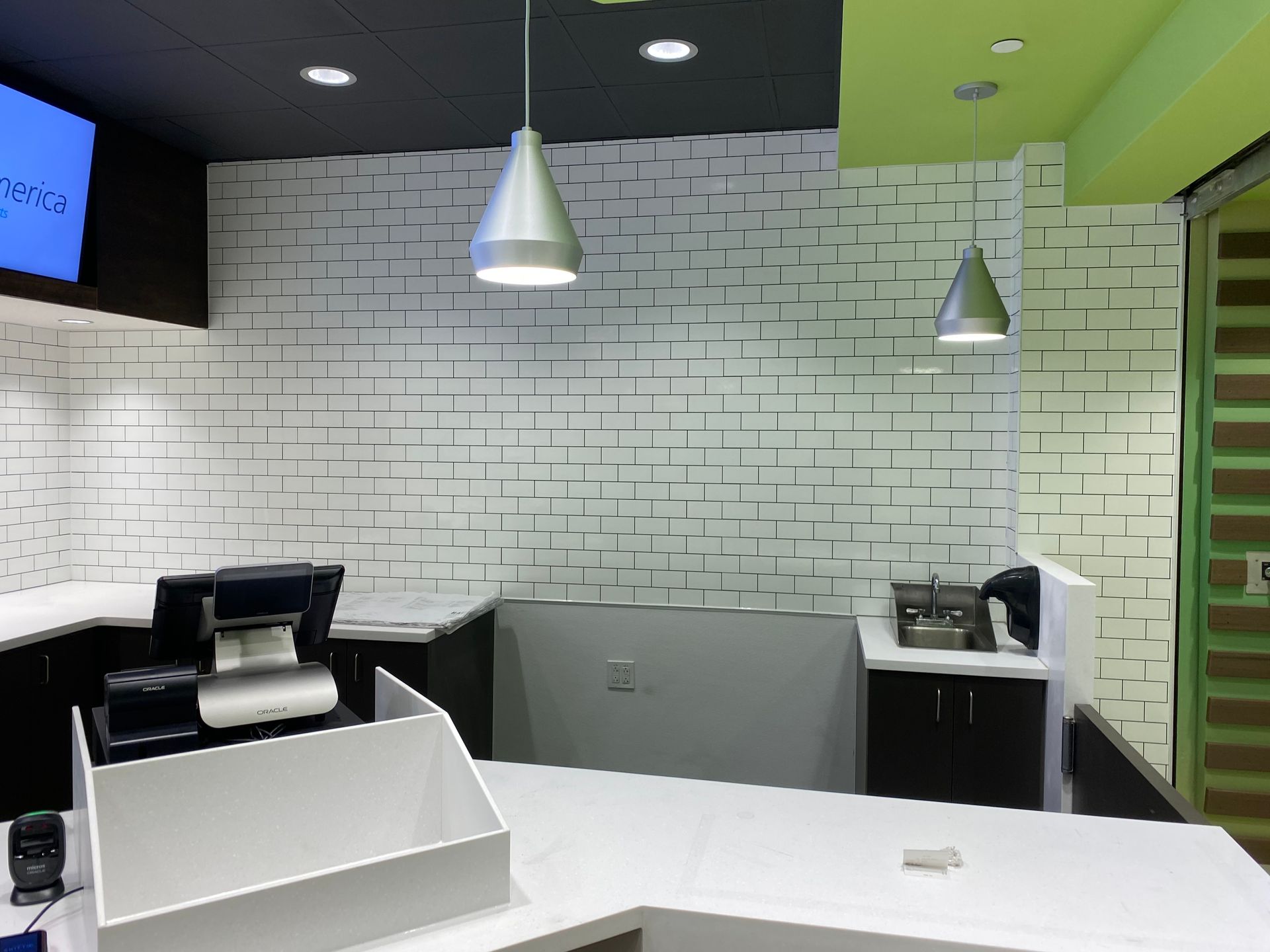 Cashier counter with white brick-patterned wall, two hanging lights, and point-of-sale system.