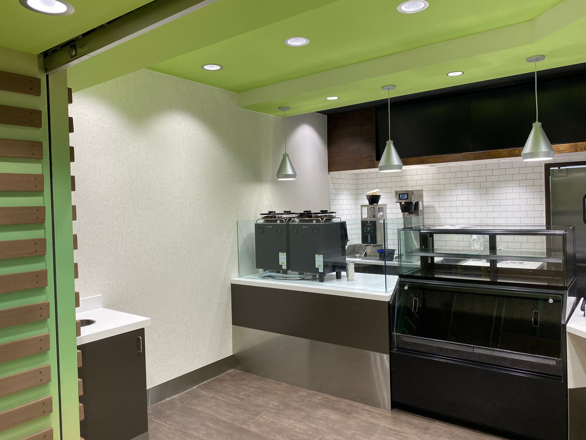 A coffee shop interior featuring a counter, equipment, and overhead lighting; green and white walls.