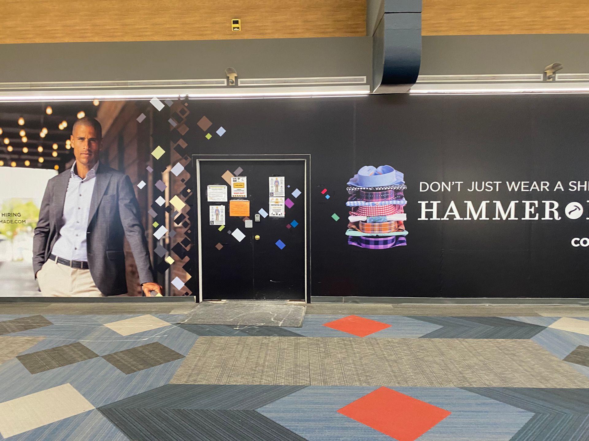 Man in suit next to door, a Hammer+Shirts ad with colorful shirts on a black wall.