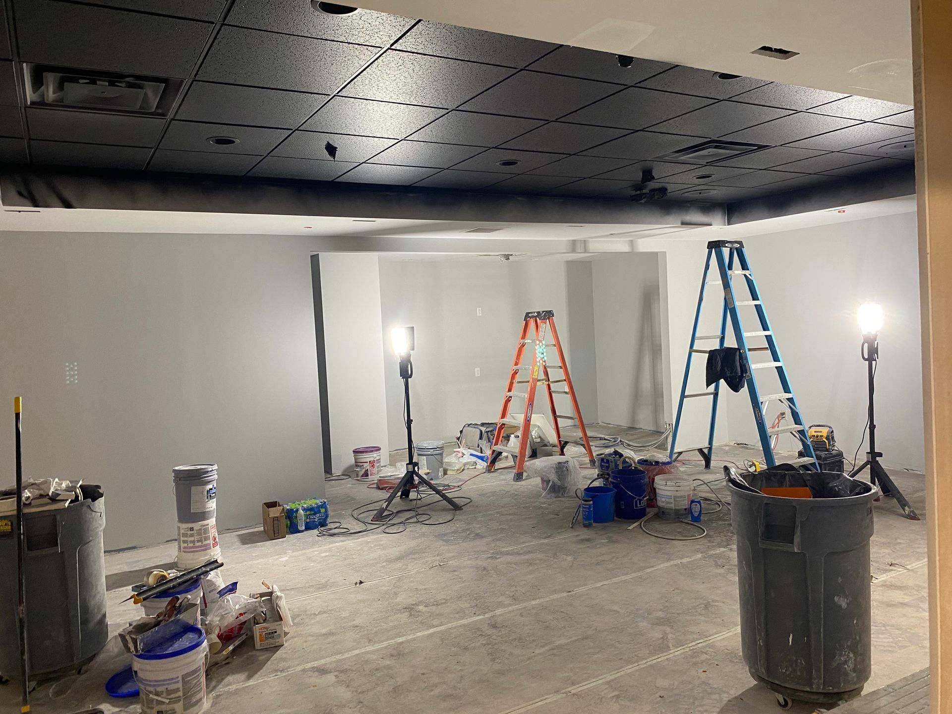 Room under renovation with gray walls, black ceiling, ladders, and painting supplies.