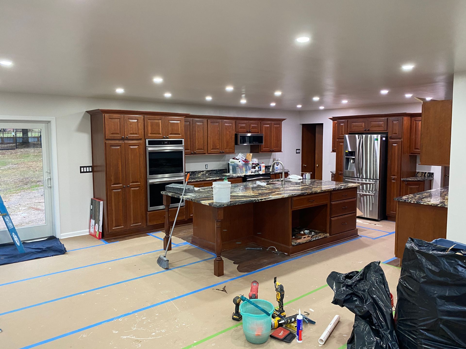 Kitchen renovation with brown cabinets, island, stainless steel appliances, and protective floor covering.