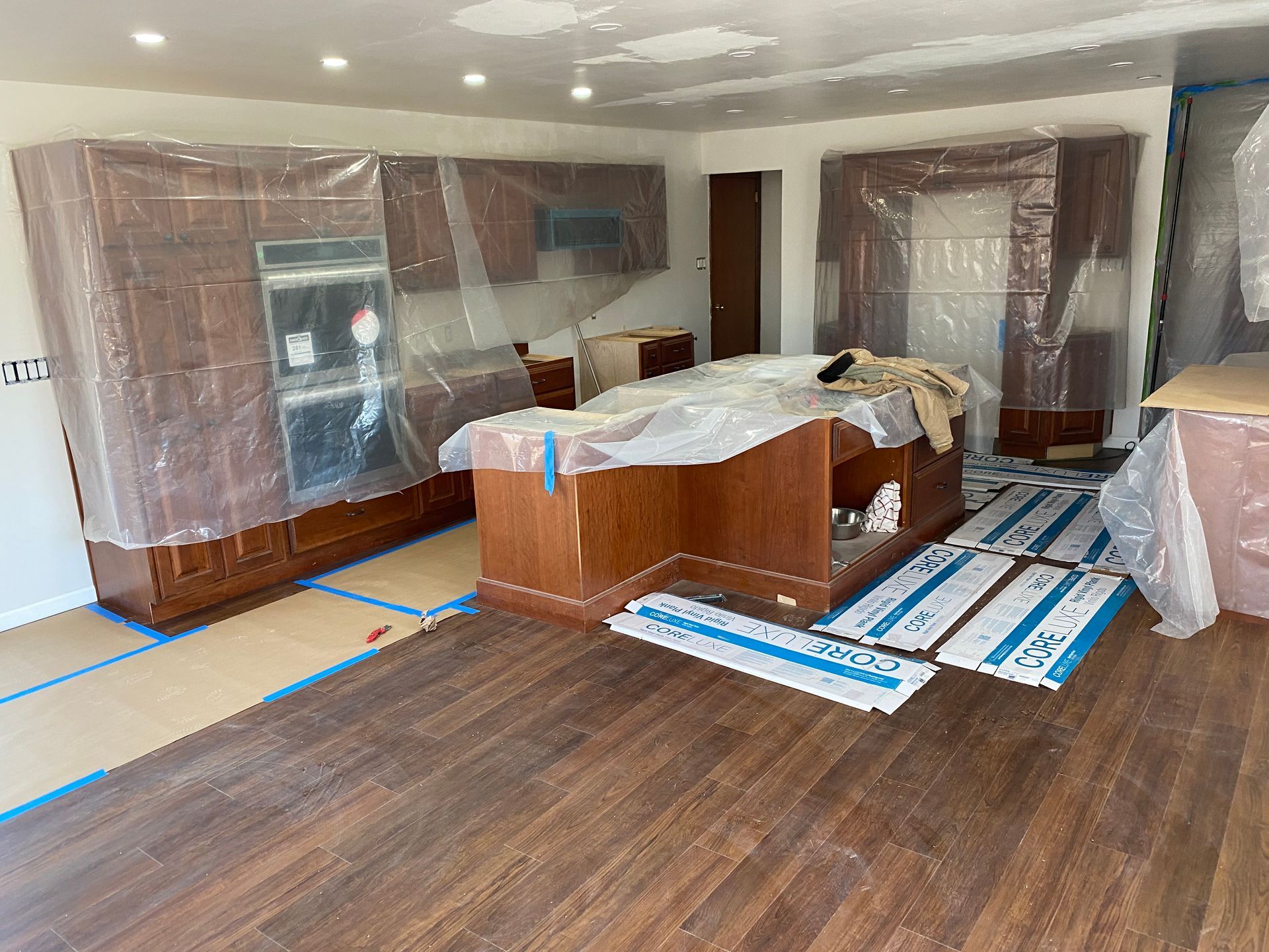 Kitchen with cabinets and island covered in plastic for protection during renovation; wood flooring.