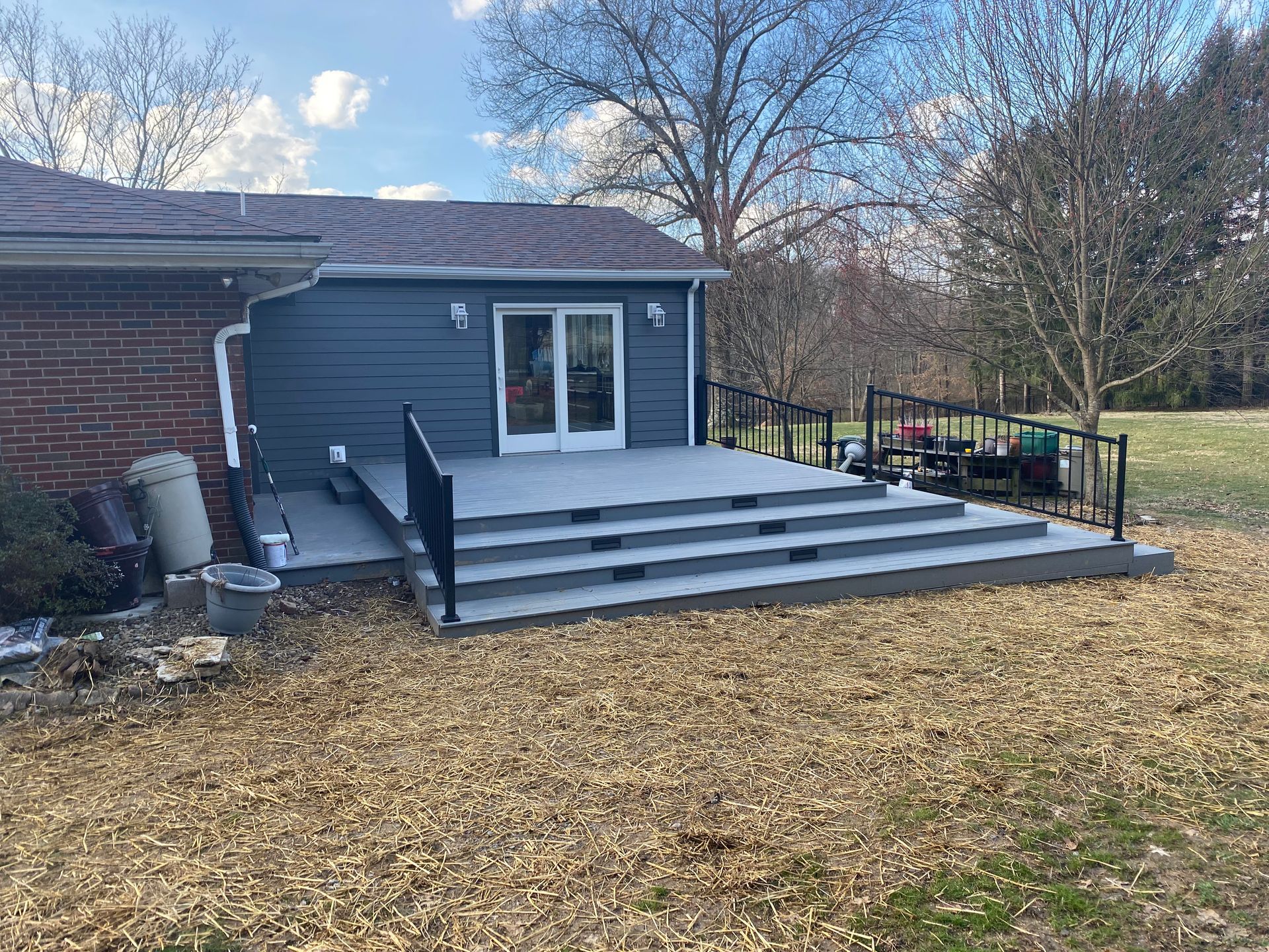 Exterior of a house with a gray deck and ramp leading to a gray and blue structure with glass doors.