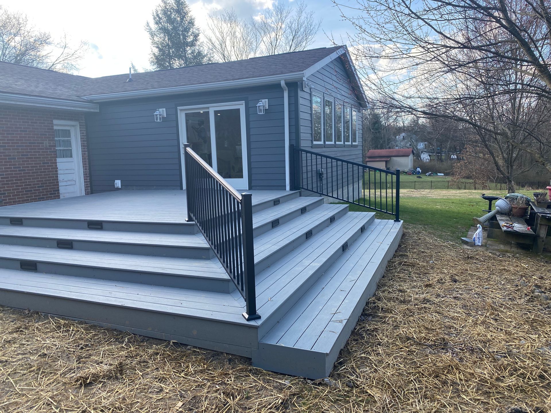 Gray deck with black railing and steps leading to a dark gray house with windows and a door.
