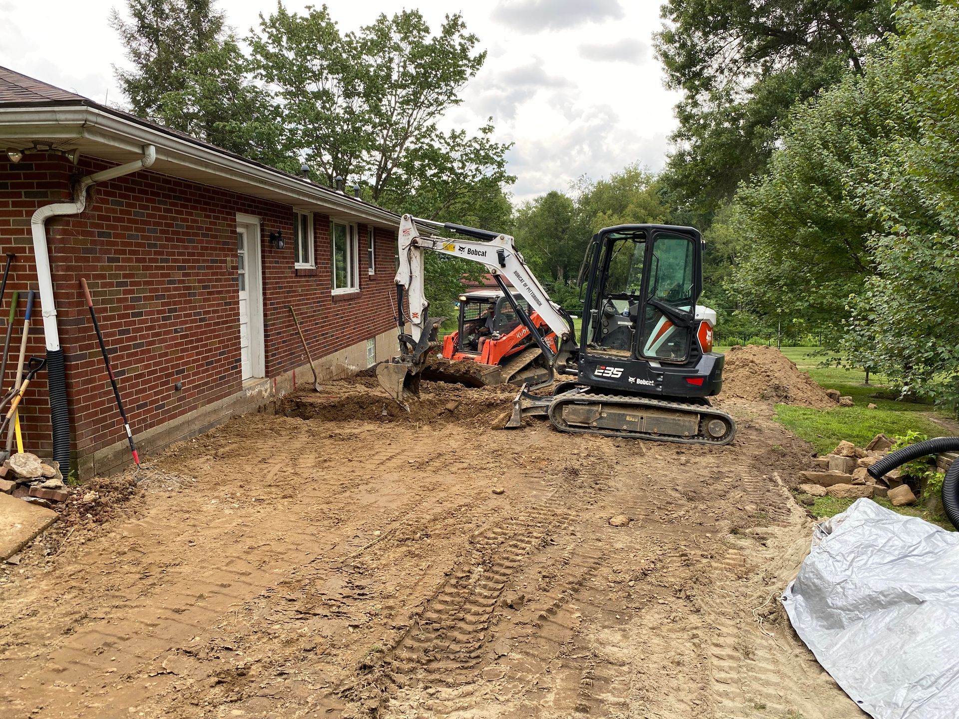 Two excavators digging near a brick building. Earthmoving equipment on a construction site.