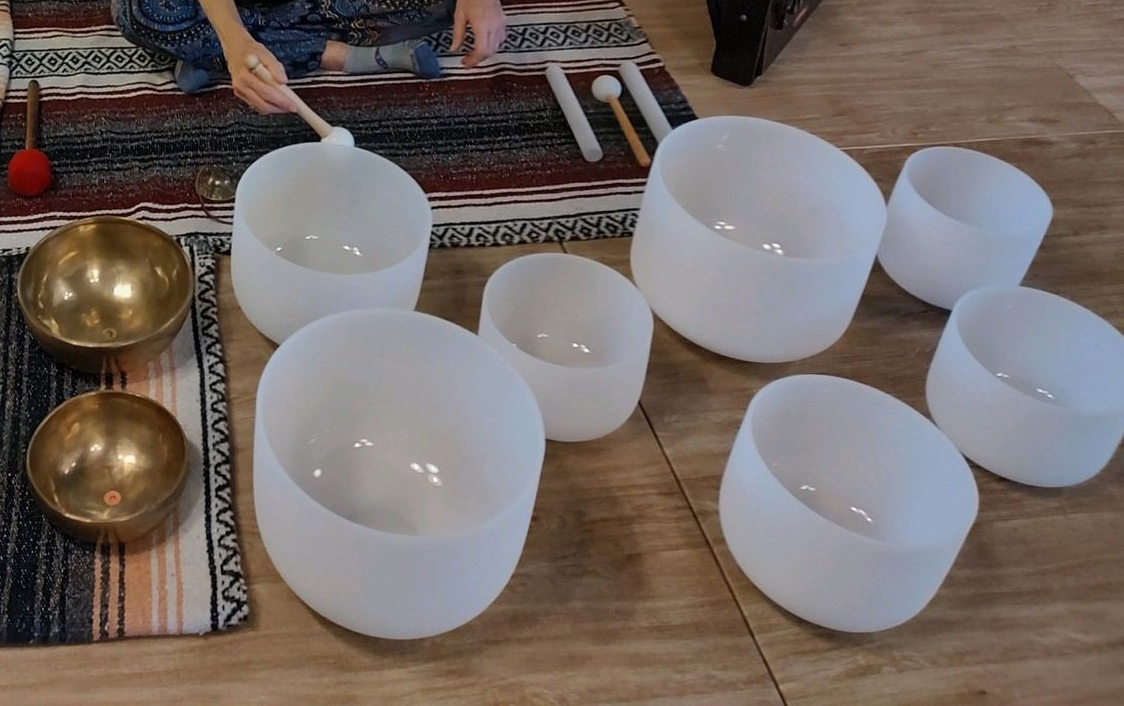 A person is playing a set of singing bowls on a wooden floor.