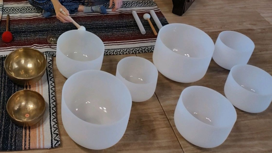 A person is playing a set of singing bowls on a wooden floor.