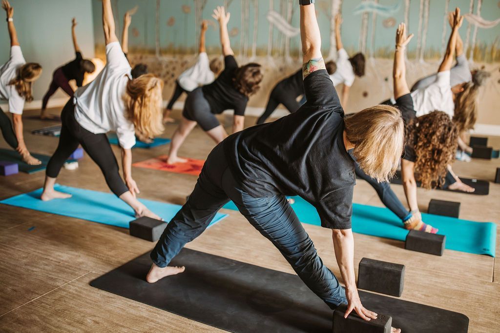 People doing yoga in a studio, arms raised; blue mats; neutral expressions.