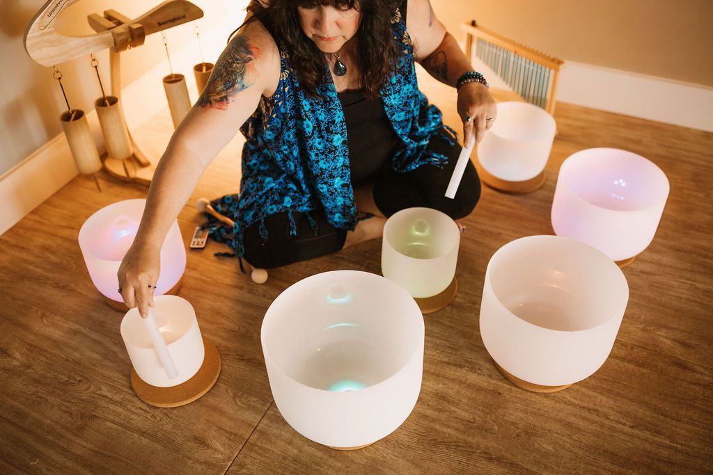 Woman playing crystal singing bowls, softly lit room, holding a mallet.
