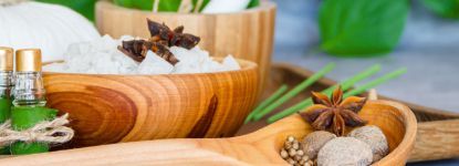 A wooden bowl filled with salt and spices next to a wooden spoon.