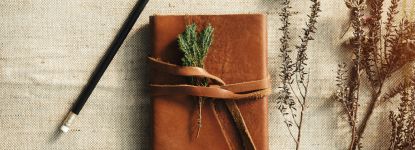 A brown leather notebook with a pencil and flowers on a table.