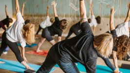 People doing yoga in a studio, arms raised; blue mats; neutral expressions.