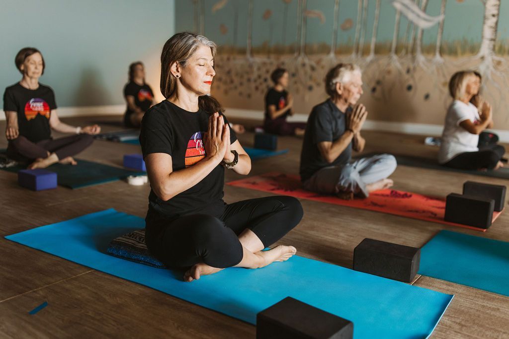 People seated on yoga mats in a studio, meditating with hands at their chests.