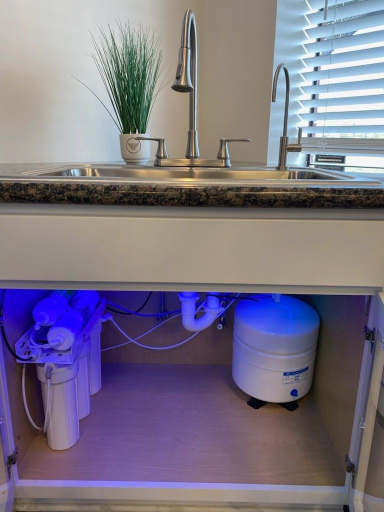 A kitchen cabinet with an under-sink water filter system. The system glows blue with pipes.