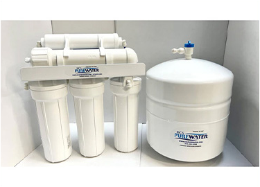 A white water filter is sitting next to a white tank.