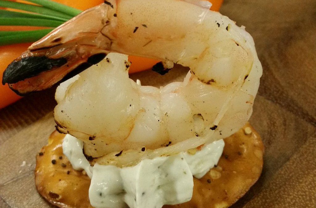 Plated shrimp canapé on a cracker with white sauce and garnish