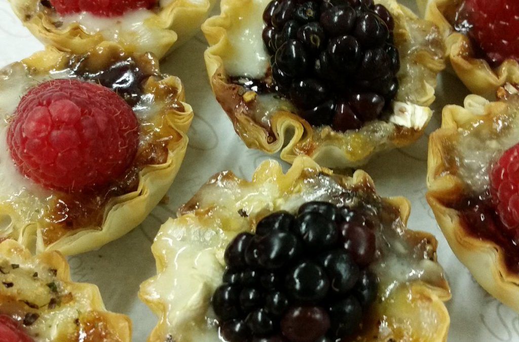 Berry-topped mini pastries on a tray, with raspberries and blackberries glazed with syrup